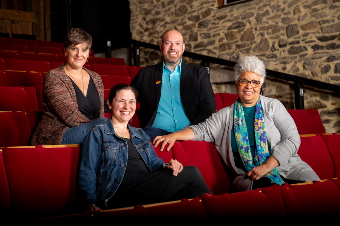 Four people sit in red theater seats, smiling at the camera.